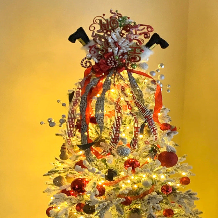 Christmas tree decorated with lights, red and white ornaments, and ribbons. The topper features festive swirls, ribbons, and decorative black boots angled upside down.