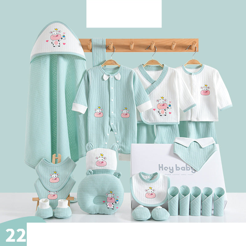 A baby gift set featuring light blue and white clothing with cow and bottle designs. Includes onesies, bibs, mittens, a hooded towel, a pillow, and washcloths displayed on a rack.