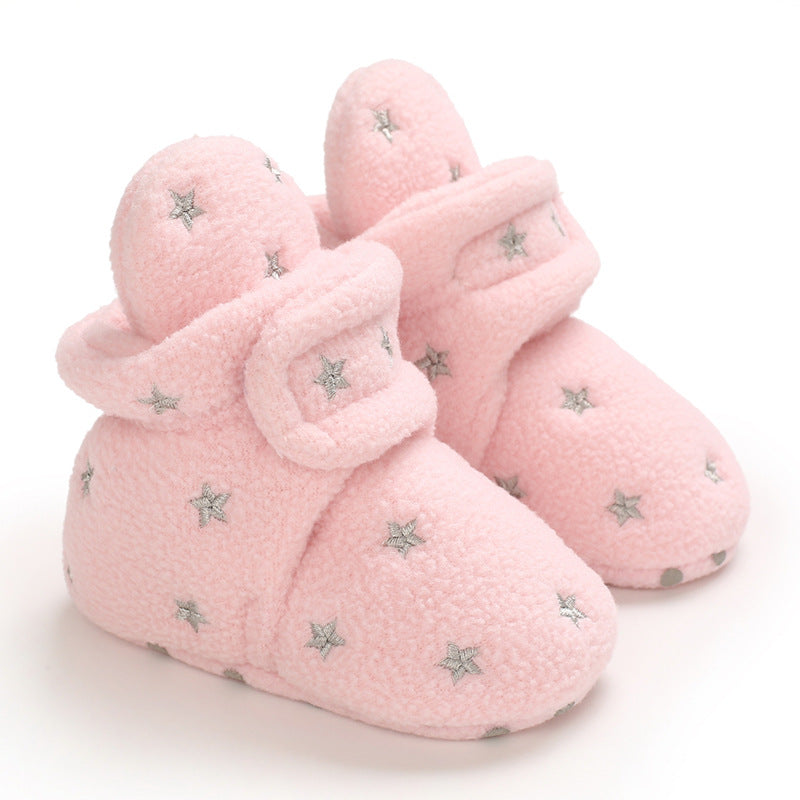 Soft pink baby booties with a fluffy texture, adorned with silver star patterns. They have fold-over cuffs for warmth and style, ideal for keeping baby feet cozy.