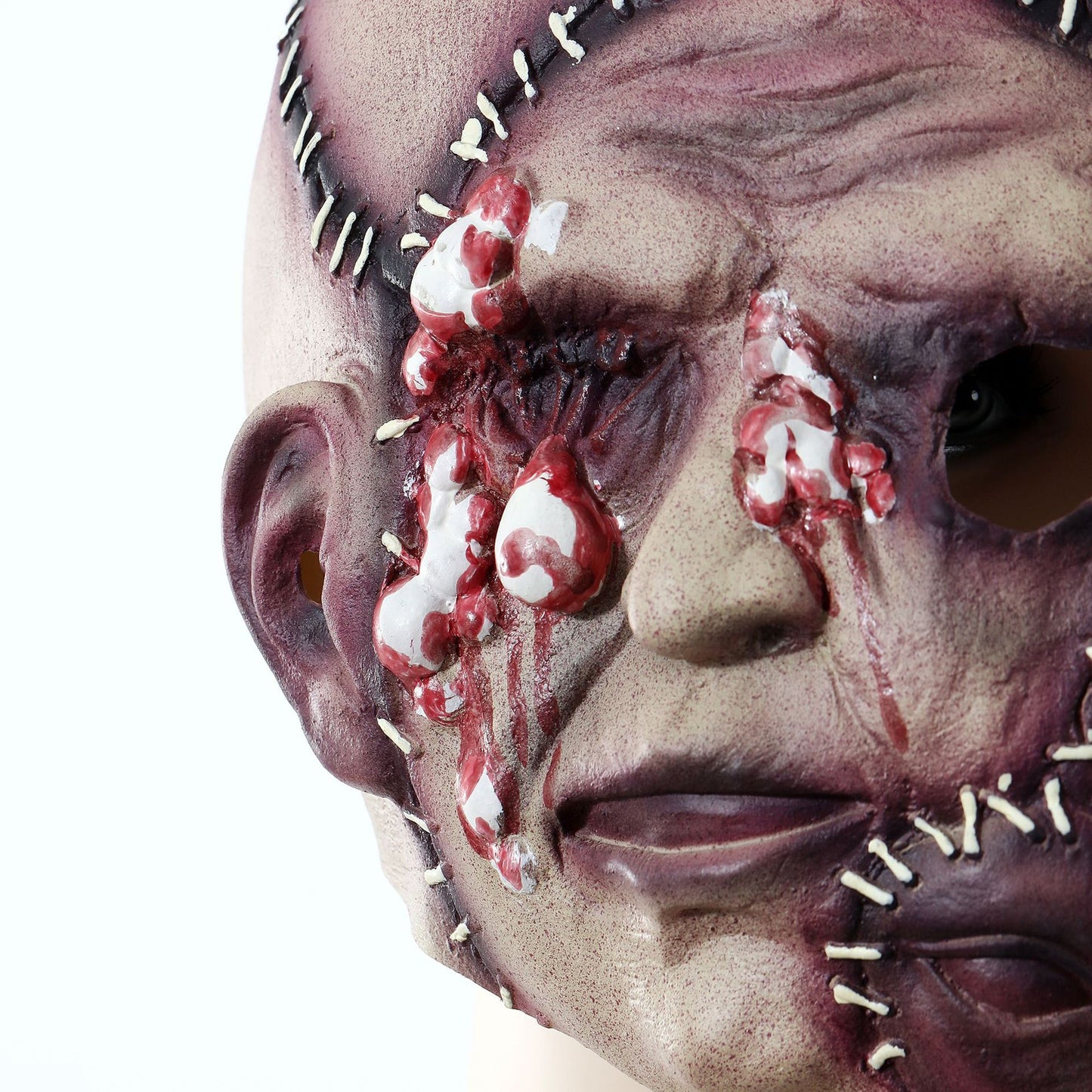 Close-up of a Halloween mask with a stitched, scarred design and blood-like details around the eye and cheek, creating a gruesome, horror-themed appearance.