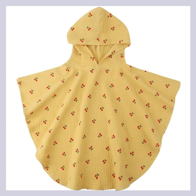 Yellow hooded cape with small red cherry patterns scattered across the fabric, displayed on a flat surface. The cape has a soft texture and a simple, cute design.