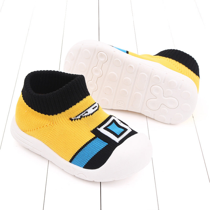 Yellow and black toddler slip-on shoes with cartoonish design and blue accents, featuring flexible white soles with circular grips, displayed on a white wooden floor.