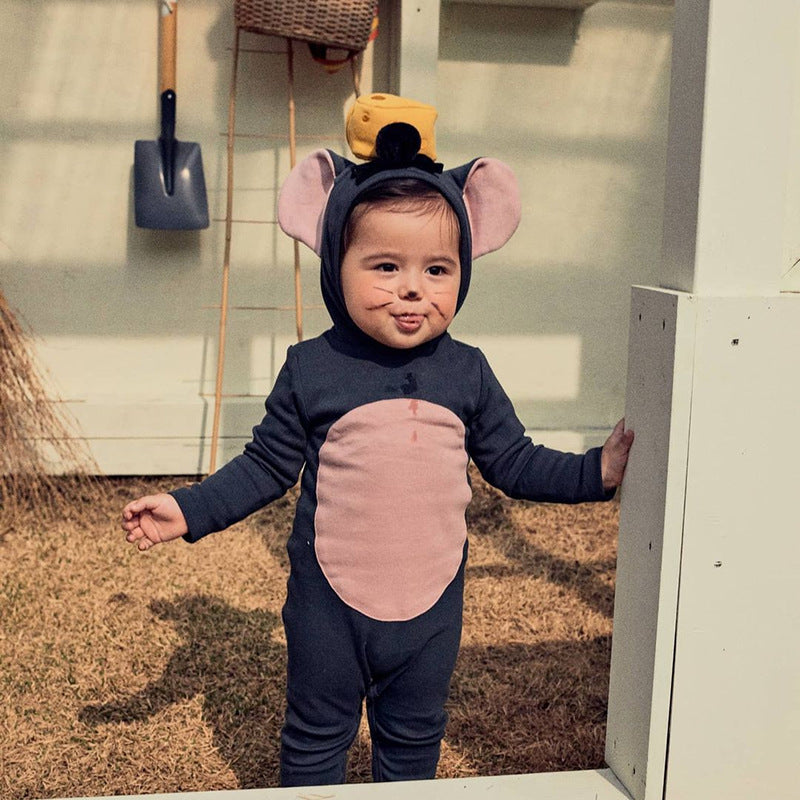 A child in a cute mouse costume with large ears and a cheese hat stands outside on grass, making a playful expression. A shovel and basket are visible on the wall behind.