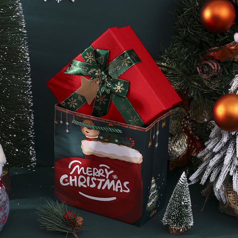 Christmas gift box with "Merry Christmas" text, featuring a red gift wrapped with a green bow. Surrounded by festive decorations, including ornaments and mini trees.