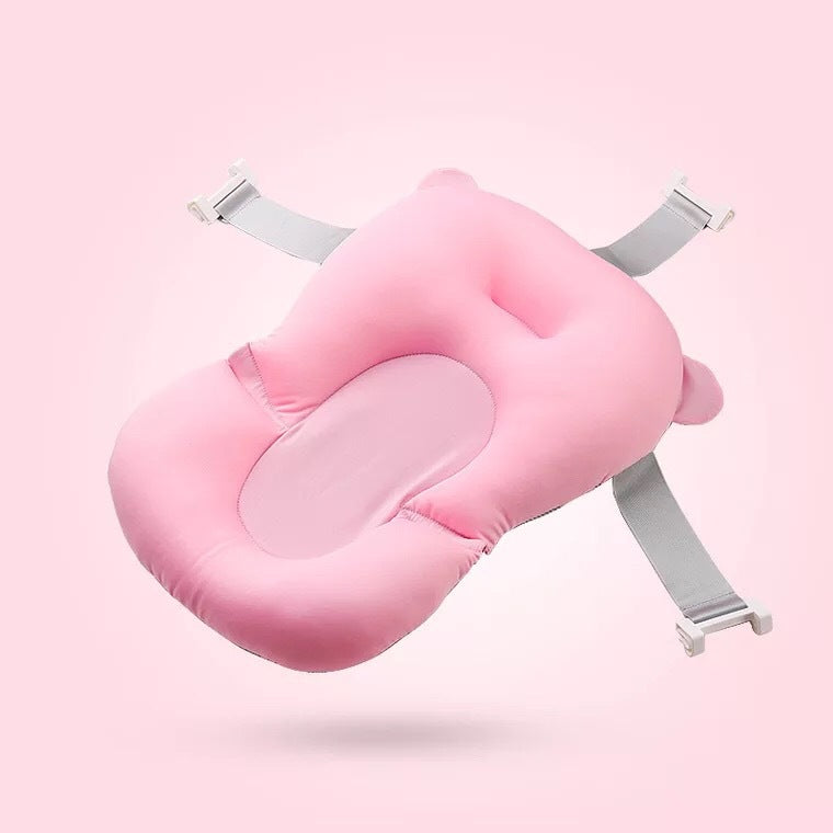 A pink baby bath cushion with a headrest and four adjustable straps, set against a matching pink background.