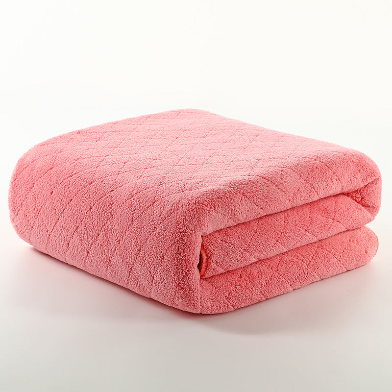 Folded pink blanket with a soft, fluffy texture and subtle diamond pattern, resting on a plain white surface.