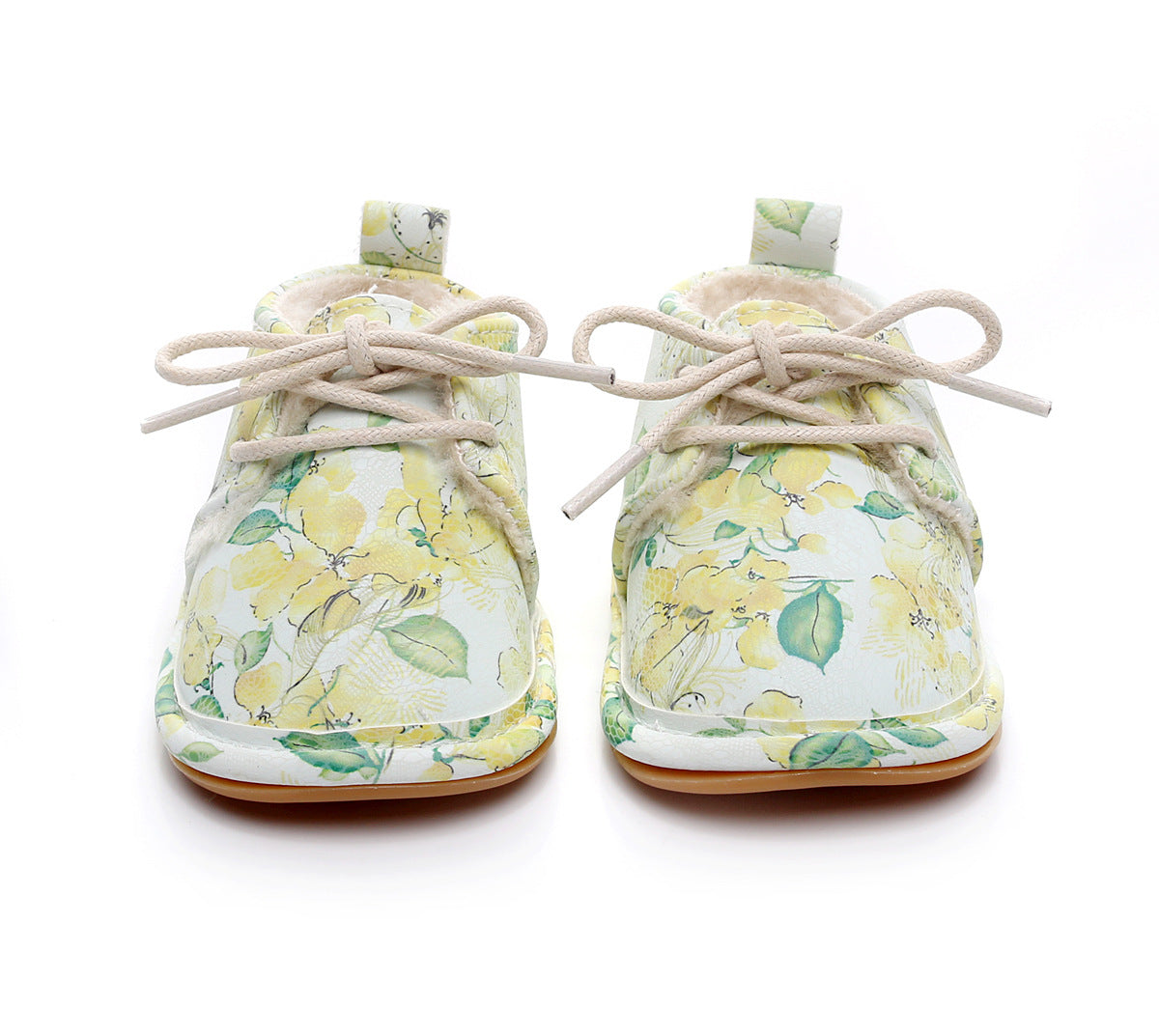 Baby shoes with a floral pattern featuring yellow flowers and green leaves, laced with beige strings. The soft, light-colored sole complements the delicate design.
