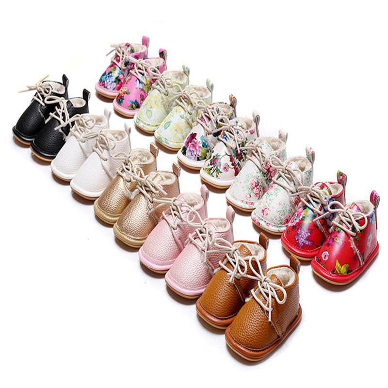 A collection of colorful baby shoes displayed in rows. Includes plain, floral, and patterned designs in various colors like black, white, gold, pink, red, and brown.