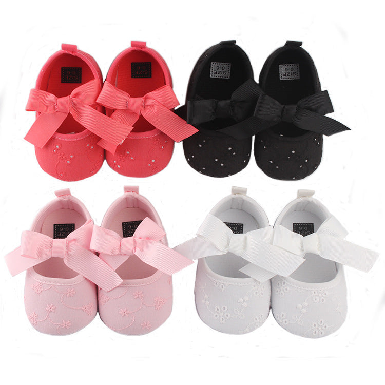 Four pairs of baby shoes with large bows on each. Colors include red, black, pink, and white. The shoes are arranged in two rows, each with detailed floral embroidery.