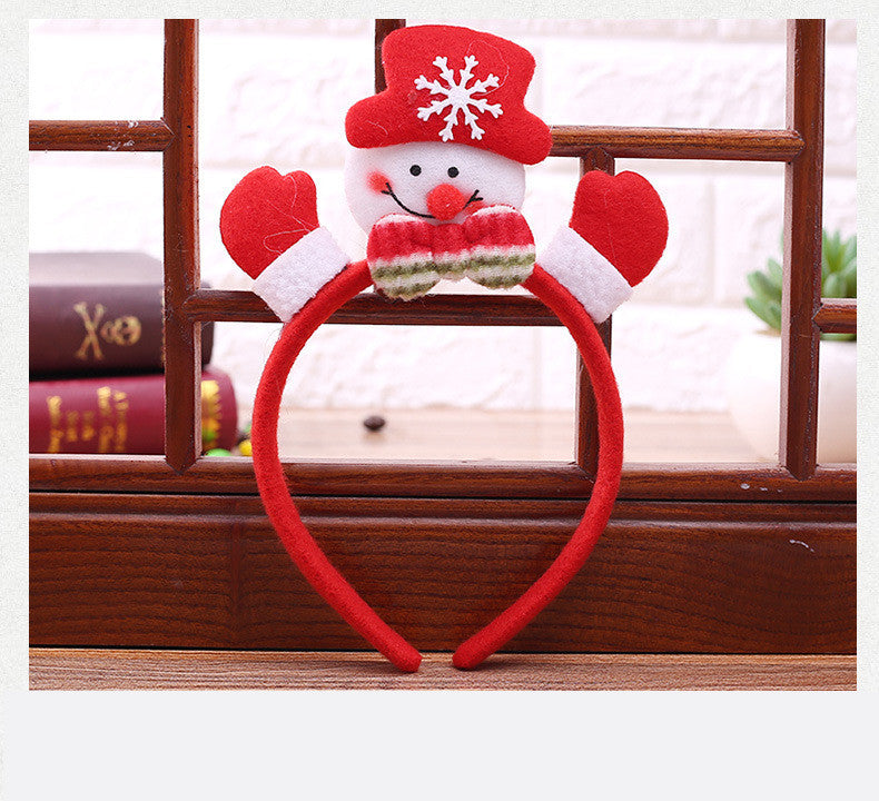 Red headband with a plush snowman design, featuring a red hat, snowflake, mittens, and a striped scarf, placed on wooden surface with books and plant in the background.