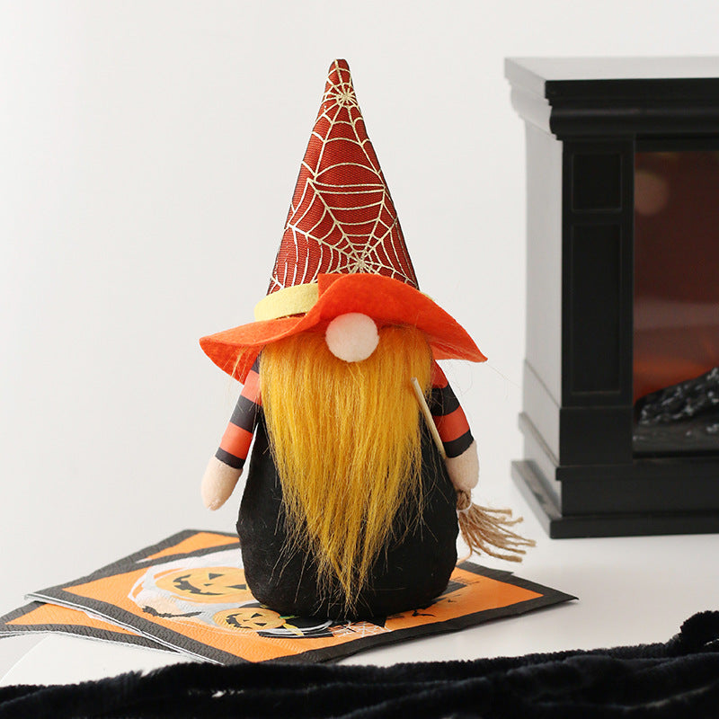 A gnome-like figure with long yellow hair wears a red witch hat adorned with a spider web pattern. It is dressed in a black outfit with orange and black striped sleeves and holds a small broom. The figure is standing on a Halloween-themed mat near a black fireplace.