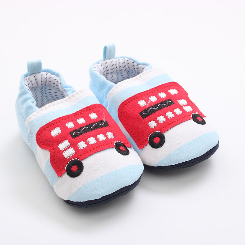 Soft baby shoes with blue and white stripes featuring a red London bus design on the front. The interior is lined with a black dashed pattern, and soles are black.