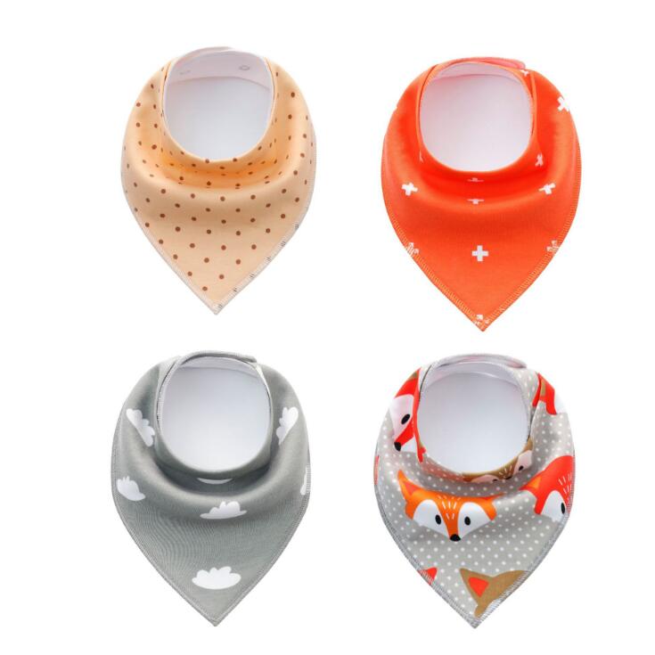 Four baby bandana bibs are arranged in a grid. Designs include beige with polka dots, orange with crosses, gray with clouds, and gray with orange foxes.