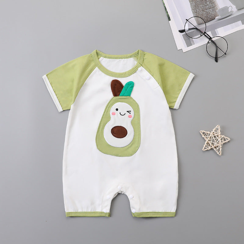 Infant romper with green sleeves and a winking pear design. Nearby are black glasses, a magazine, and a small straw star on a gray background.