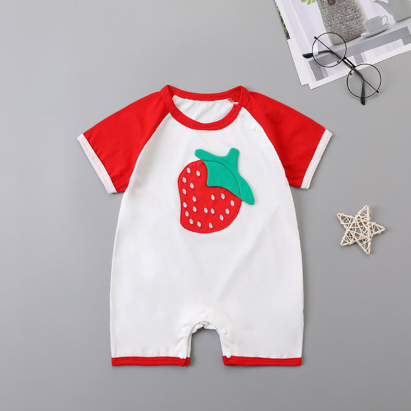 Baby romper with red sleeves and a large strawberry design on the front. It is laid out on a gray surface next to a pair of glasses, a small twig star, and a magazine.