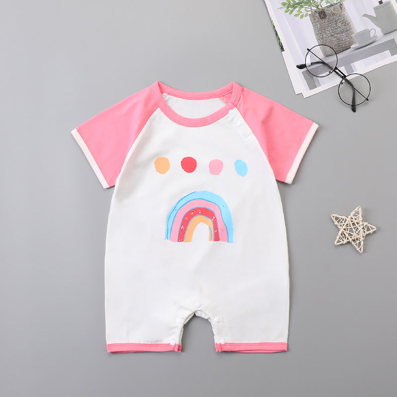 Baby romper with pink sleeves and a rainbow design on the front, laid on a gray surface. Near it are round glasses, a potted plant, and a decorative star.