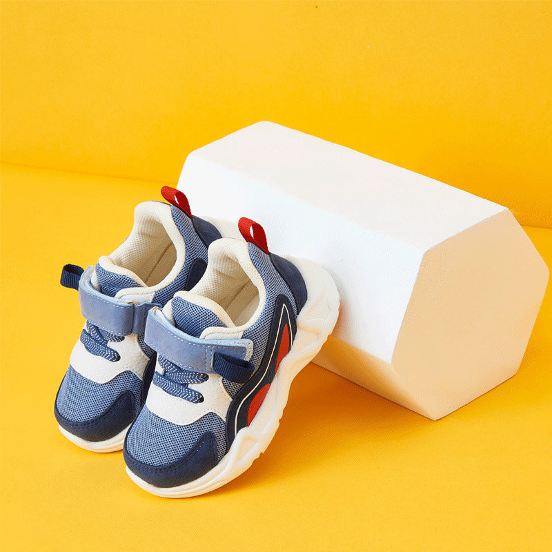 Blue and white children's sneakers with red accents resting against a white geometric block on a vibrant yellow background.