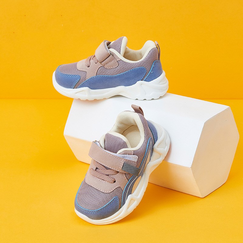 Children's sneakers with blue and beige mesh, white soles, and Velcro straps, displayed on a white block against an orange background.