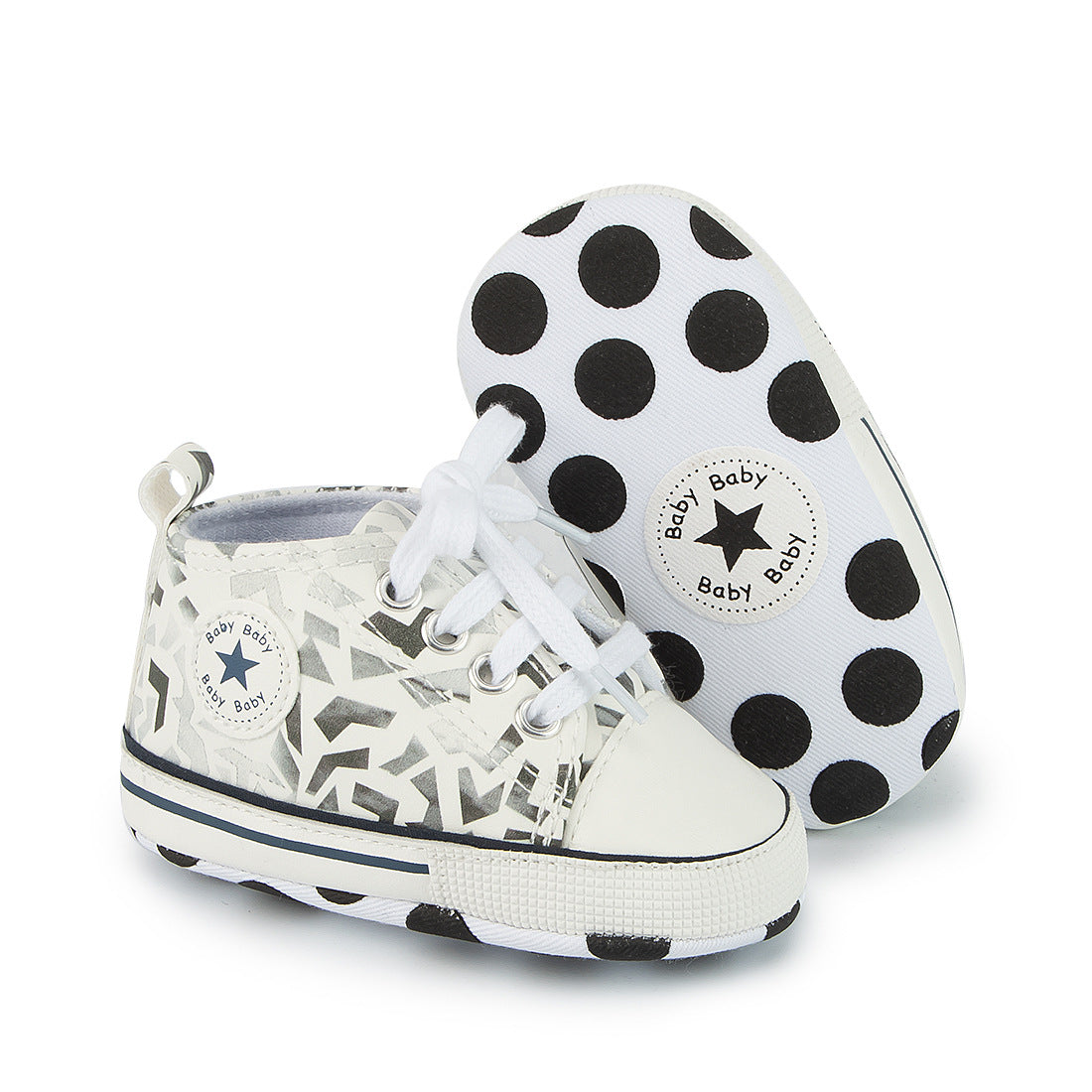 White baby shoes with black geometric patterns and star details. The sole features large black polka dots and a circular emblem with the word "Baby" and a star icon.