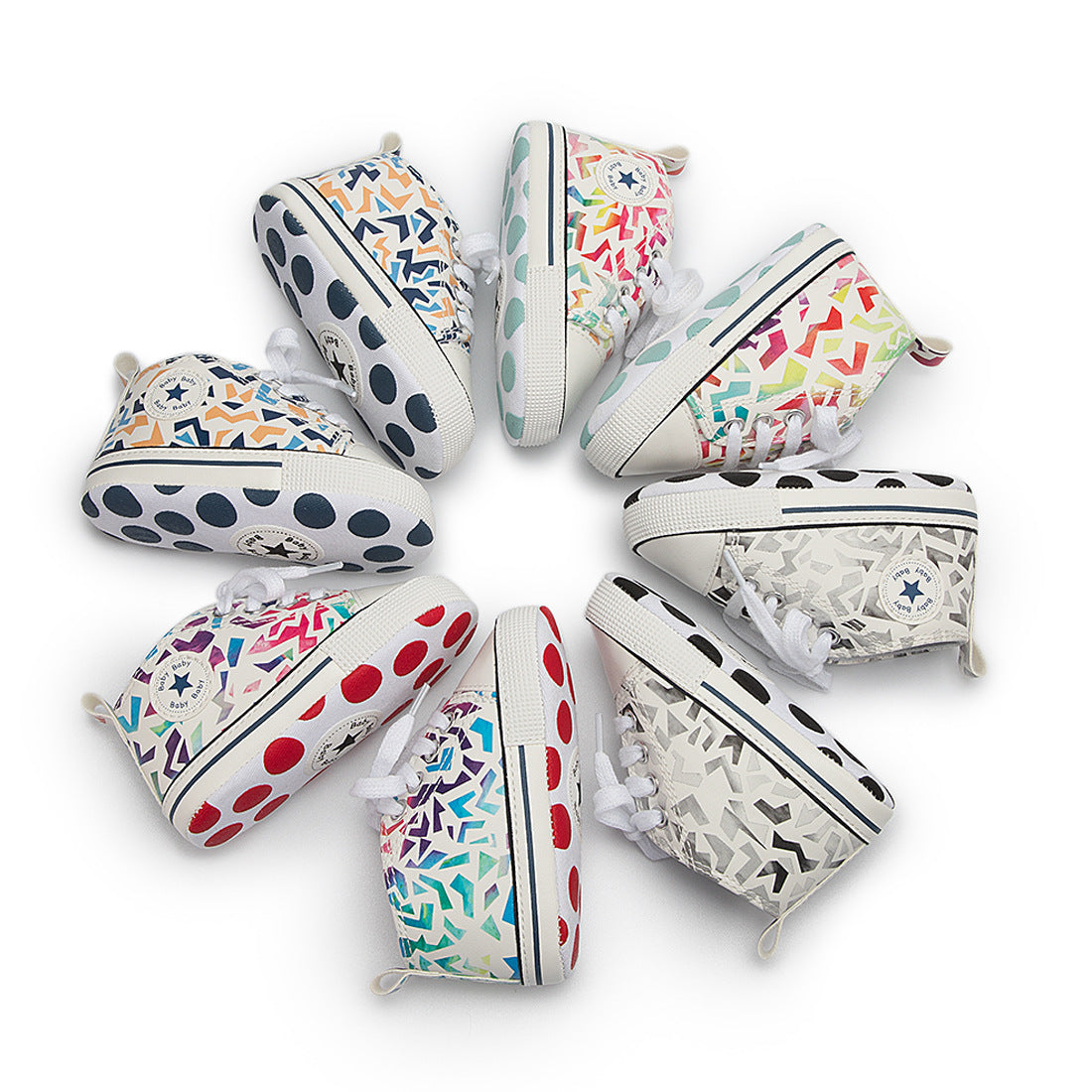 A circle of baby sneakers with colorful geometric patterns and polka dot soles in various shades, arranged radially on a white background.