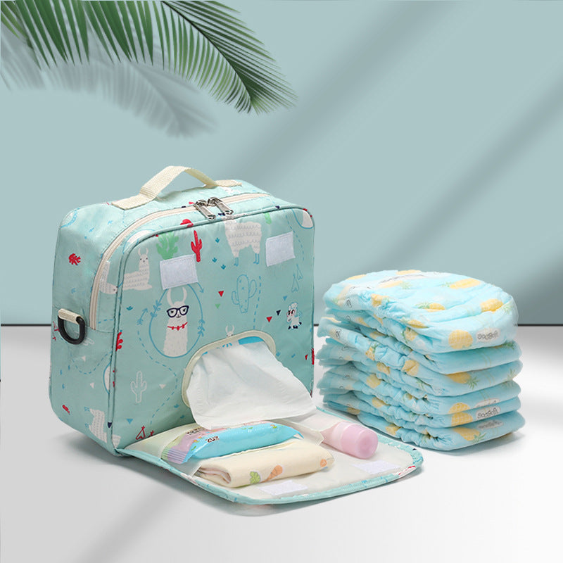 A light blue diaper bag with llama and cactus designs is open, showing wet wipes, baby lotion, and diapers. A stack of folded diapers is beside the bag.