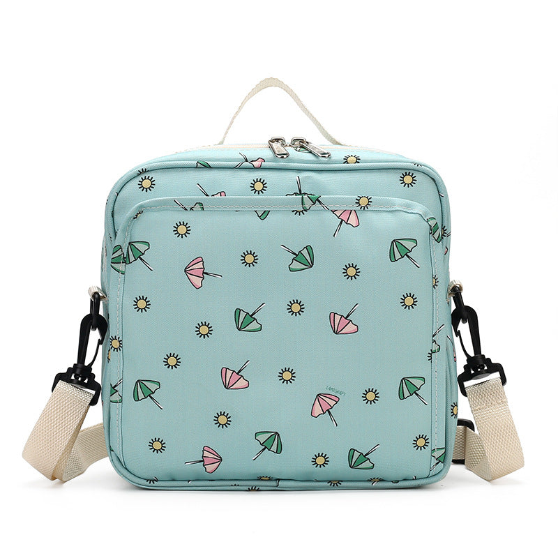 Light blue square backpack with a pattern of small green and pink umbrellas and sun shapes. Features beige straps and a top handle, with zipper closure on top.