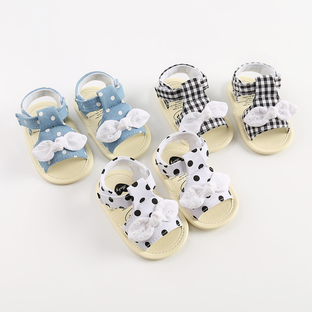 Three pairs of baby sandals are displayed: blue with white polka dots, black gingham, and white with black polka dots. Each pair features a decorative white bow.