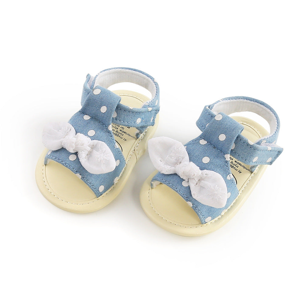 Baby sandals with blue polka dot straps, adorned with white bows, on a beige sole.