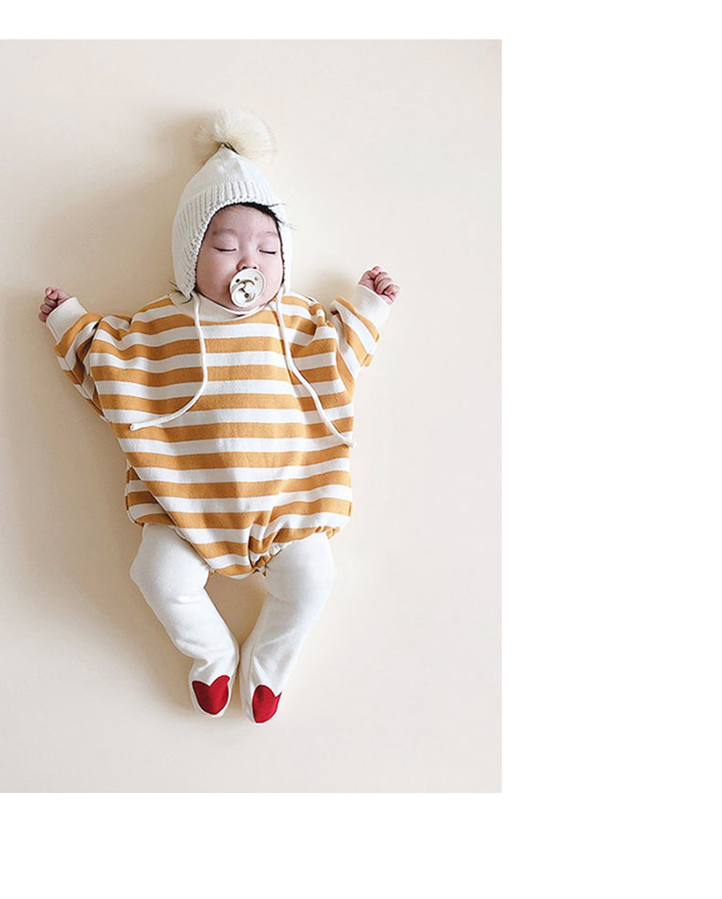 A sleeping baby in a tan and white striped outfit with a white knit hat and pacifier, wearing white socks with red hearts, resting peacefully on a light background.