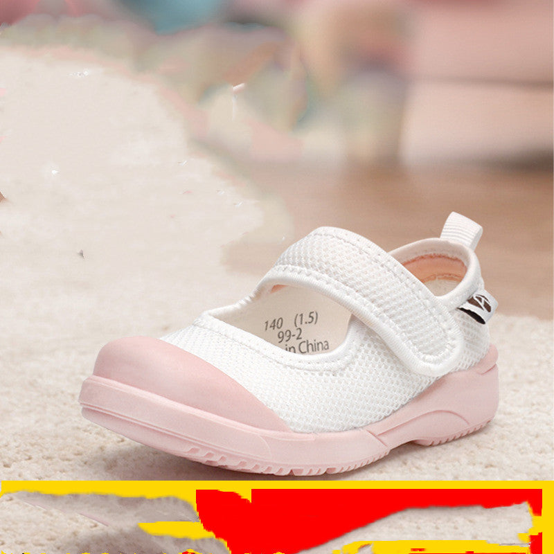 A small white children's shoe with a pink rubber toe and sole, featuring a breathable mesh upper and a hook-and-loop strap, sits on a light carpeted surface.