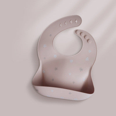 Pink silicone baby bib with small white star patterns, featuring an adjustable button closure and a wide catch pocket. The bib is set against a soft, neutral background.