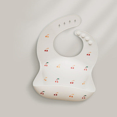 White silicone baby bib with cherry print pattern, featuring an adjustable neck strap with five fasteners and a built-in pocket to catch spills.