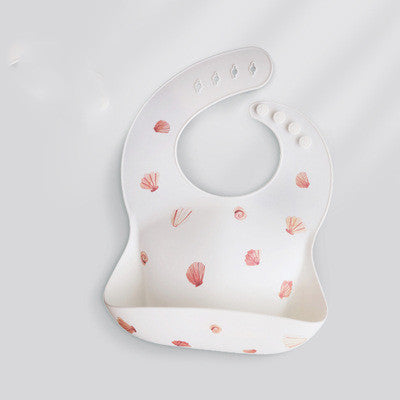 White silicone baby bib with pink seashell pattern, featuring adjustable buttons and a food-catching pocket at the bottom.