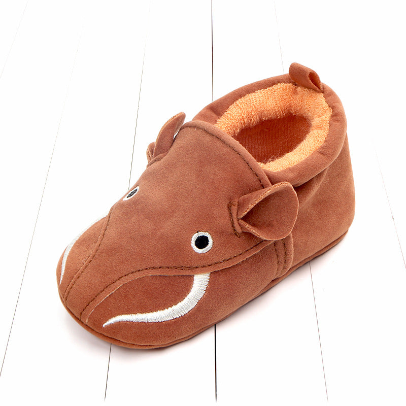 Brown children's slipper designed as a cartoon mammoth with embroidered eyes and tusks, set on a white, wooden surface.