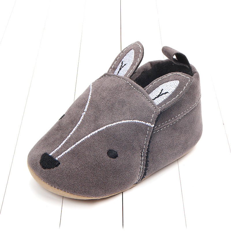Gray suede baby shoe styled as a mouse, with embroidered facial features and small ears. The shoe is placed on a white wooden surface.