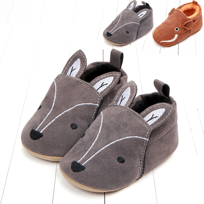 Gray baby slippers shaped like deer with stitched faces and ears, on a light wooden floor. A smaller gray and a brown animal slipper are placed above them.