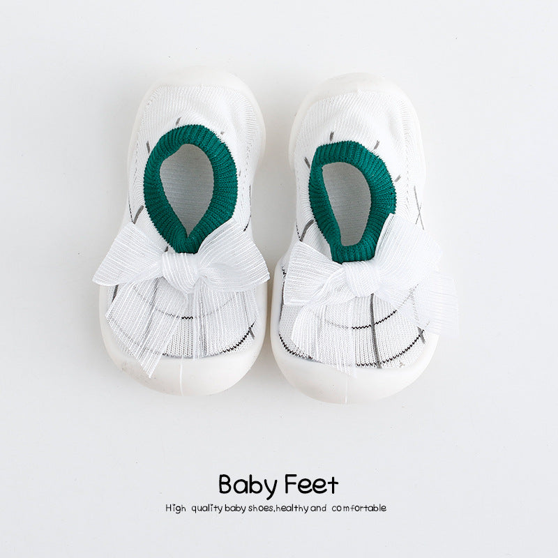 White baby shoes with green trim and white ribbon bows, placed on a plain background. The text below reads "Baby Feet," emphasizing quality, comfort, and health.