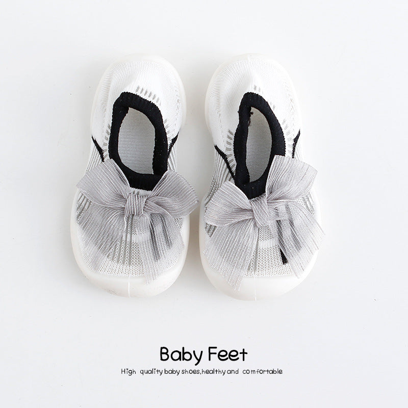 White baby shoes with black trim and large gray bows on top. The text below reads "Baby Feet" and describes them as high-quality, healthy, and comfortable footwear.