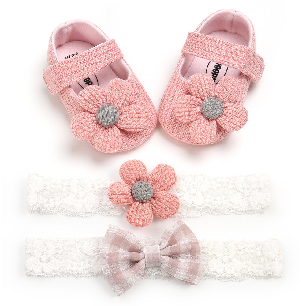 Pink baby shoes with large flower appliques, paired with two lace headbands: one with a pink flower and another with a pink and white checkered bow, on a white background.