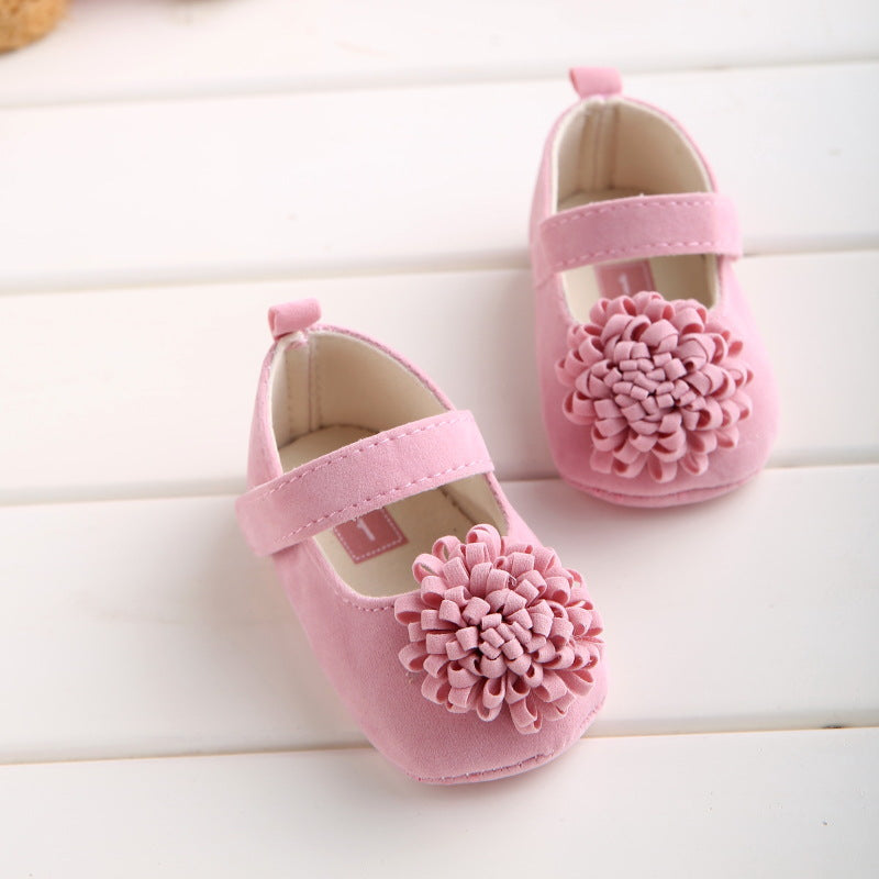 Pink baby shoes with a flower embellishment on each toe, featuring a Mary Jane strap, displayed on a white surface.