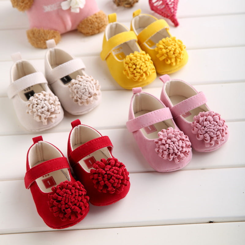 Four pairs of colorful baby shoes on a white surface, each featuring a flower embellishment. They are red, pink, yellow, and white, arranged neatly in a row.