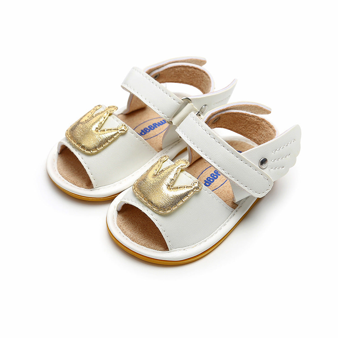 White baby sandals with gold crown embellishments, featuring wing-shaped design on straps. Peep-toe style set against a white background.