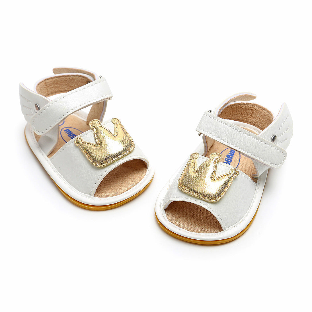 White baby sandals with adjustable straps and gold crown decorations on the front. The interior is tan, and the soles are beige with a slight heel.