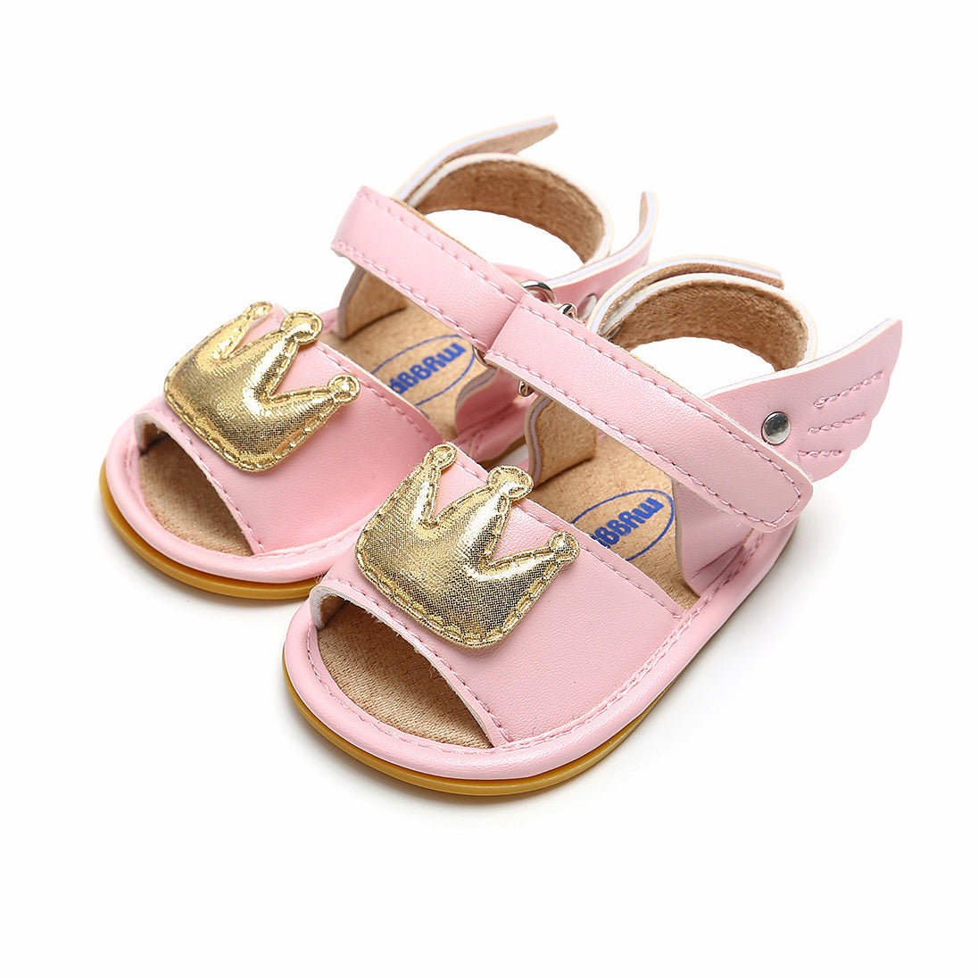 Pink baby sandals with gold crown embellishments on the straps and small wing accents on the sides, featuring an open-toe design with light brown soles.
