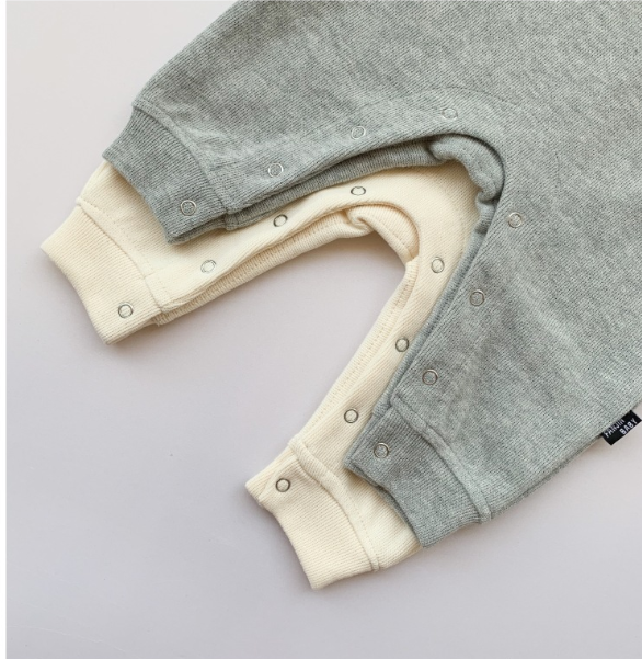 Two baby onesies with snap buttons lie on a surface. One is light gray, the other cream-colored. Both have ribbed cuffs and a soft texture.