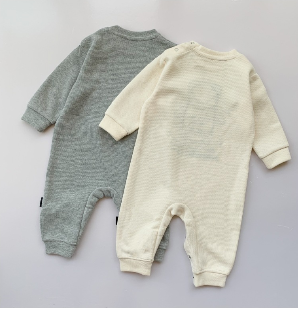 Two baby onesies laid flat, one gray and one cream-colored. The gray one is plain, and the cream one has a faint pattern. Both have long sleeves and snap closures at the shoulders.