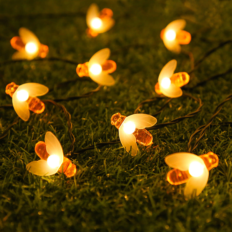 String lights shaped like fireflies glowing warmly on grass, featuring orange bodies and white wings.