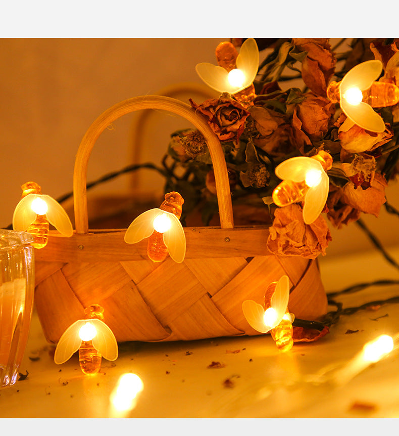 A woven basket adorned with glowing bee-shaped string lights and dried flowers on a warm-lit surface.
