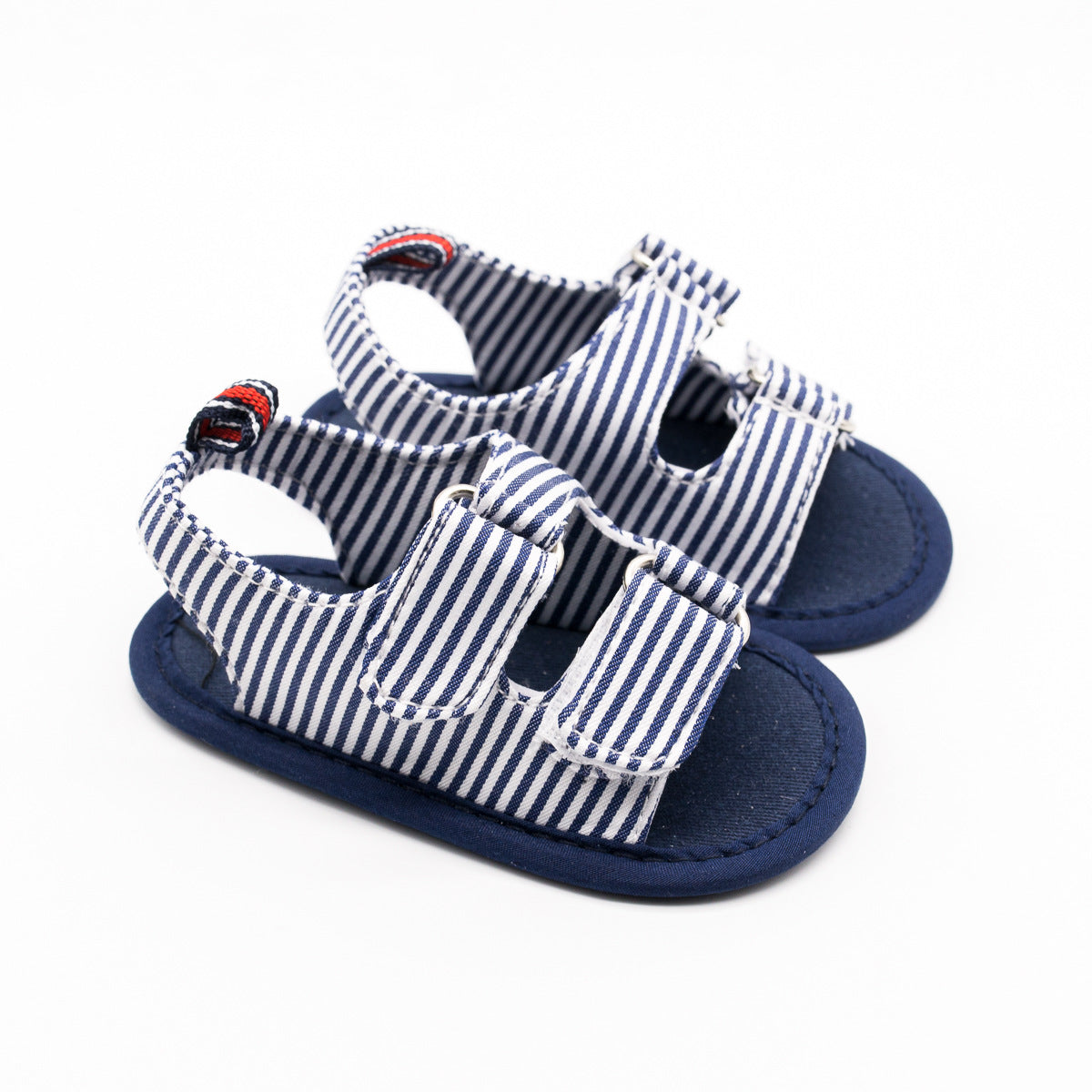Blue and white striped baby sandals with navy soles and velcro straps, featuring red and black stitching on the back loops, placed against a plain white background.
