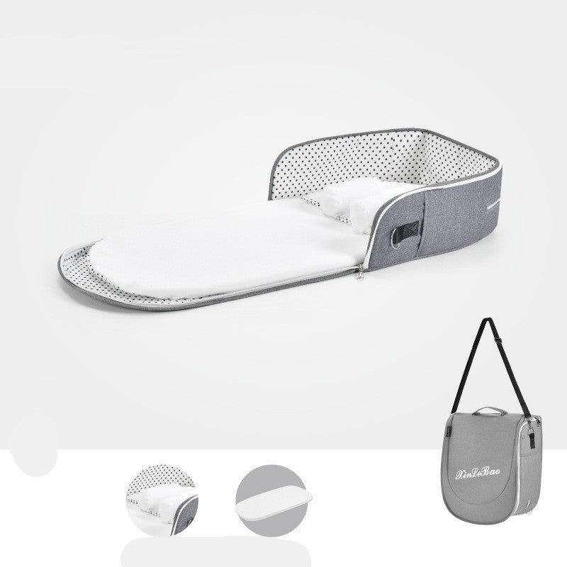 Portable baby bassinet with a white cushioned interior and gray polka dot sides, featuring a zip-up design. Includes a matching gray carry bag with a shoulder strap.